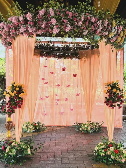 An elegant backdrop for an engagement or Roka ceremony, featuring peach-colored drapes and a beautiful arch of pastel flowers.