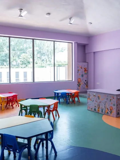 This classroom uses a soothing lavender wall color and features a large window for natural light. The modular, colorful tables can be arranged in various configurations to support different activities, from group work to individual art projects.