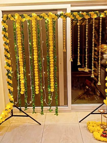 Even a simple setup can be beautiful. Here, I used a metal frame decorated with yellow marigold garlands, hanging bells, and delicate fairy lights to create an intimate and glowing space for a small pooja.