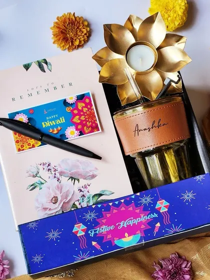A modern and useful Diwali gift for the younger generation. This hamper includes a personalized water bottle with a leather sleeve, a floral notebook, a pen, and a lotus-shaped brass diya.
