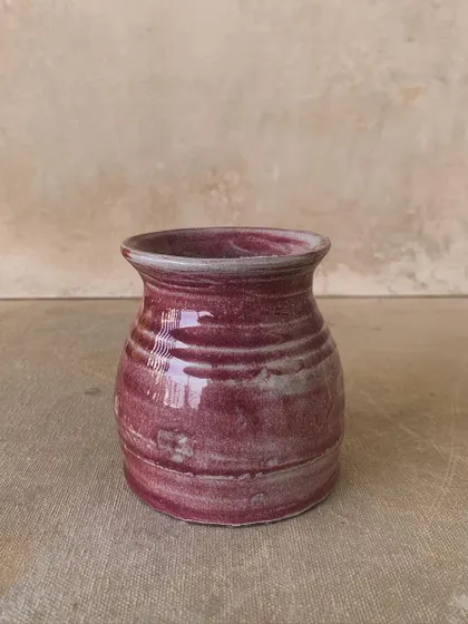 A small, rustic pot with a rich magenta glaze. The imperfect shape and texture are what give this piece its unique charm.