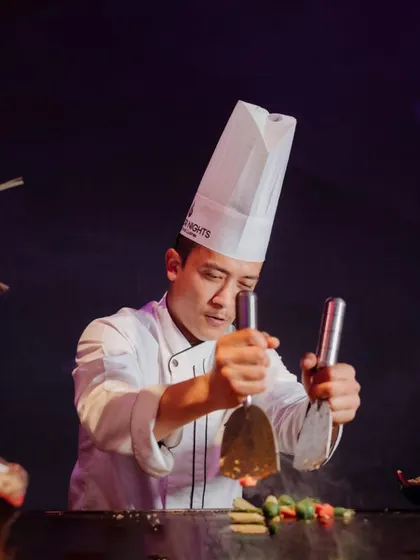 A chef showcases his teppanyaki skills at a live station, engaging guests with precision and flair. This is a perfect entertainment addition for corporate events.
