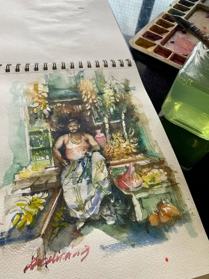 Another view of my morning sketch of the banana seller, showing the piece in my sketchbook next to my watercolor palette. It's a snapshot of my creative process.