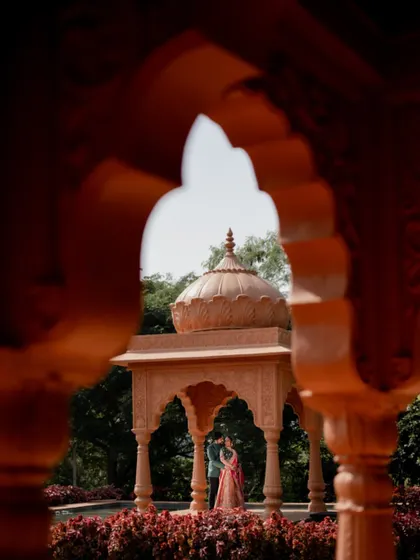 A creative shot framing the couple and the gazebo through an archway, adding depth and a sense of discovery to the pre-wedding photograph.