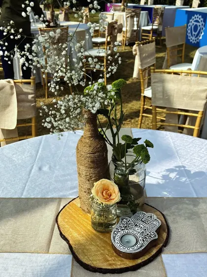 A rustic-chic centerpiece combining a twine-wrapped bottle, a Hamsa Hand candle holder, and fresh flowers on a wooden slice, blending spiritual and bohemian elements.