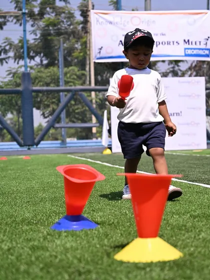 A toddler concentrates on scooping a ball and placing it in a cone.
