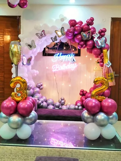 A close-up of the 32nd birthday home setup, showing the details of the balloon arch with chrome pink and silver balloons, butterfly stickers, and a neon sign.