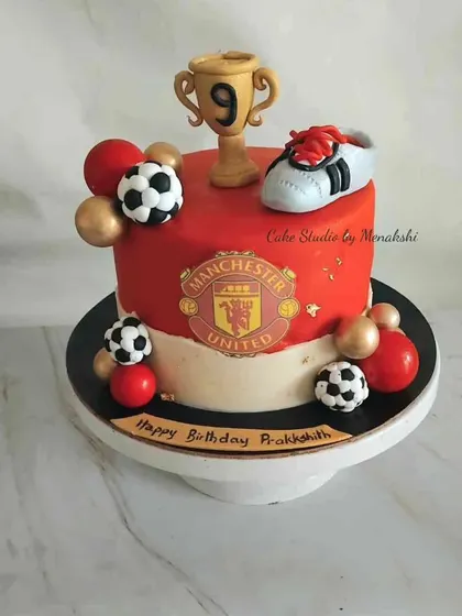 For a Manchester United fan. This cake is decorated in the team's colors and features their crest, a trophy, a football boot, and soccer balls.