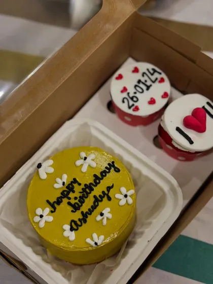 A bright and sunny birthday combo with a yellow bento cake decorated with white daisies. The two cupcakes continue the theme with personalized messages like "26-01-24" and a simple "I ❤️ U".