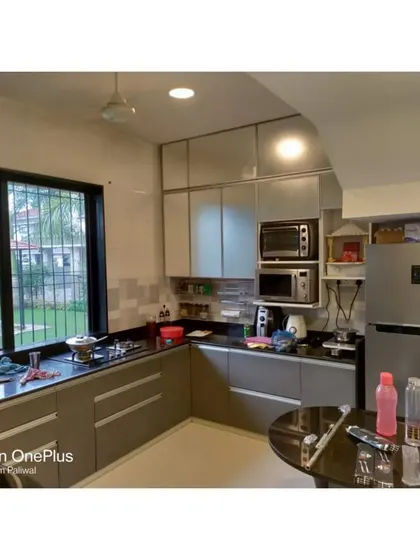 This L-shaped kitchen for Mr. Maheshwari uses a combination of solid and profile shutters. The layout provides an efficient work triangle and integrates the refrigerator and microwave oven neatly.