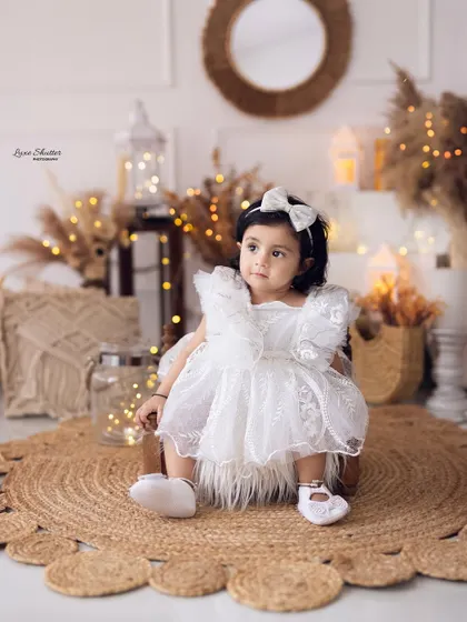 A lovely seated portrait of the birthday girl in her white dress, surrounded by a warm, rustic, and beautifully lit boho setup.