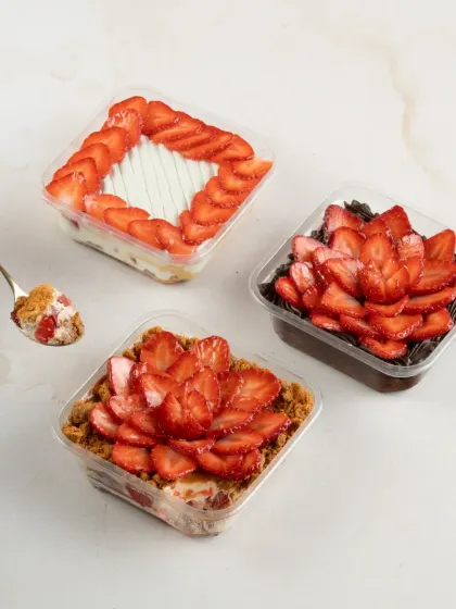 Dig into our made-to-order desserts loaded with fresh strawberries. Pictured here are our Strawberry Biscoff Cheesecake, Strawberry Tres Leches, and Traditional Chocolate Strawberry Gateau tubs.