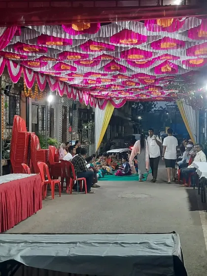 An outdoor event space with a decorated pandal ceiling. Guests are seated on the floor and on chairs, showing a flexible arrangement.