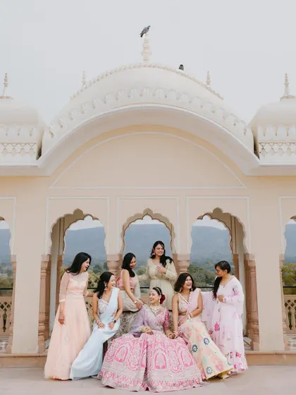 An elegant portrait of the bride seated with her bridesmaids against the backdrop of a beautiful palace dome and arches.