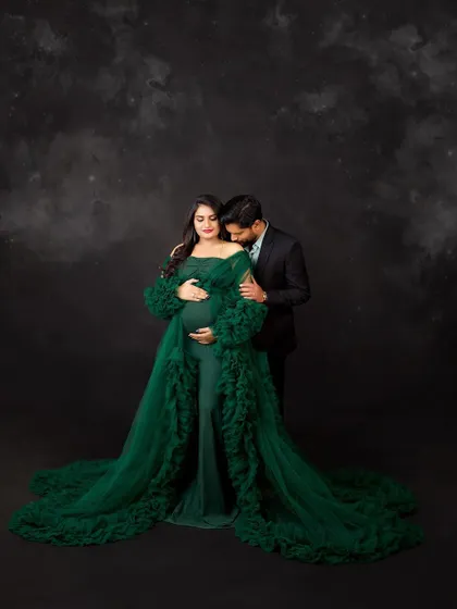 A tender moment captured in a magical setting. The husband's gentle kiss on his wife's shoulder adds a layer of intimacy to this enchanting, green-themed portrait.