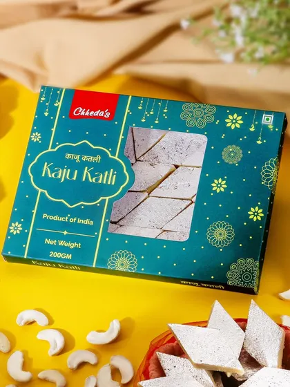 This image for Kaju Katli uses a bright yellow background to create a festive and cheerful mood. The composition highlights the attractive packaging, making it look like a perfect gift for celebrations.