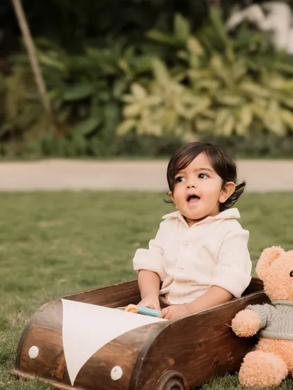 A toddler and his teddy bear companion ready for an adventure in their wooden car prop.
