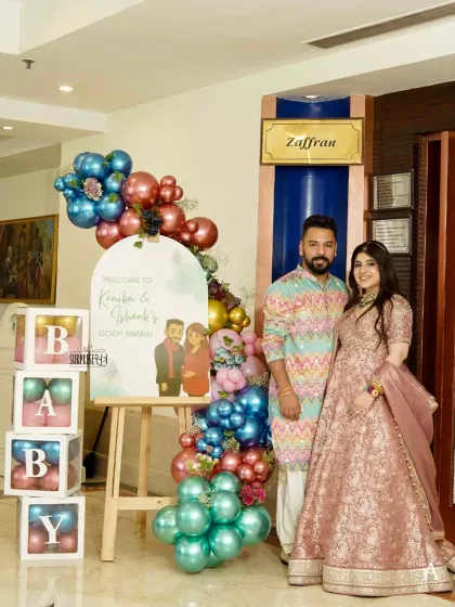 A personalized welcome to the Godh Bharai, featuring a custom caricature of the expecting couple. The jewel-toned balloon arrangement and "BABY" blocks completed the entrance decor.