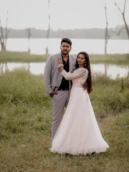 A stylish couple posing during their outdoor pre-wedding shoot. She is wearing a light pink gown with sheer, puffy sleeves, and he is in a smart grey suit.