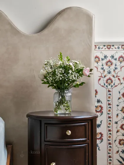 A close-up detail from the 'Room of Sukoon'. The combination of the soft, curved headboard, the dark wood nightstand, and the traditional Indian block-print inspired wallpaper creates a perfect blend of modern comfort and heritage charm.