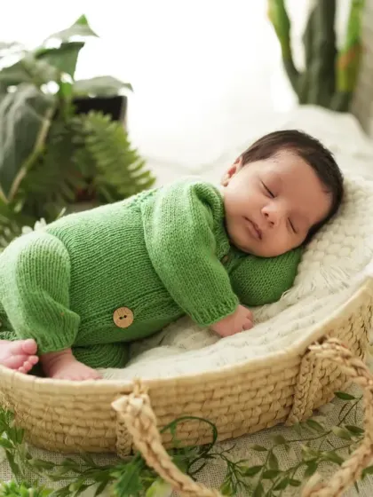 A side profile of a sleeping newborn in a green knit romper, showing the delicate features of the baby. We pay close attention to posing and lighting to create artistic portraits.