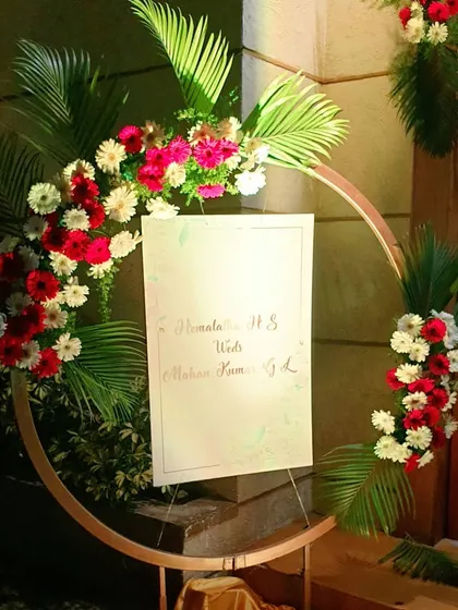 For this wedding reception, I designed a welcome sign holder using a modern, circular metal frame. The frame is decorated with bold red and white flowers and tropical palm leaves.
