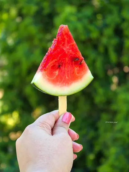 A similar shot of the watermelon popsicle, this time with a different green background, showing versatility in a simple concept. This is a great example of creative food styling.