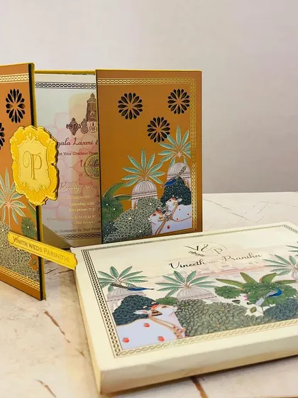 This unique invitation set features Pichwai-style art with peacocks and lotus motifs. The gate-fold card is held together by a custom acrylic nameplate.