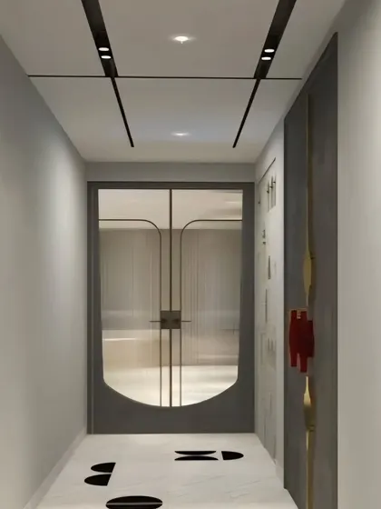 A view down a corridor with minimalist white marble flooring featuring black inlay details, leading to a modern door with fluted glass panels.
