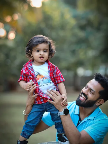 A father playfully holds his son during an outdoor photoshoot. The genuine smiles and interaction showcase a fun and natural father-son bond.