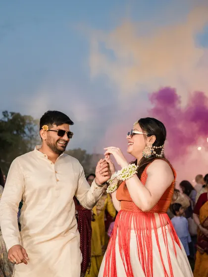 The couple dancing at their Holi-themed event, the groom in a simple yet stylish off-white kurta that allows the bride's colorful outfit to pop.