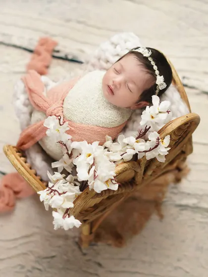 A newborn rests in a decorative wooden prop, surrounded by white flowers. I use a variety of props to create unique and artistic compositions for each baby's photoshoot.