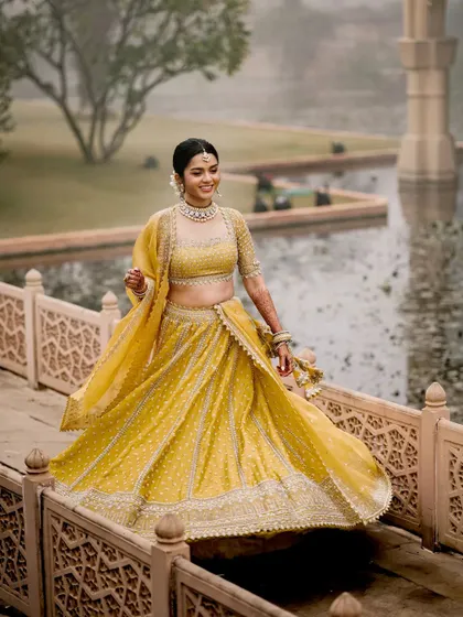 A beautiful action shot of the bride twirling in her vibrant yellow lehenga on a bridge at the palace. This captures the joy and elegance of the bride during her pre-wedding festivities.