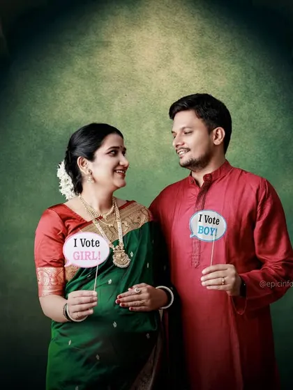 "Team Boy" or "Team Girl"? This couple has fun with props during their traditional green and red saree maternity shoot.