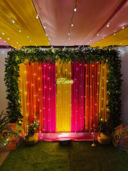The full view of the Haldi backdrop, set up on an artificial grass carpet. The decor uses bright colors and natural elements to create a garden-like feel indoors.