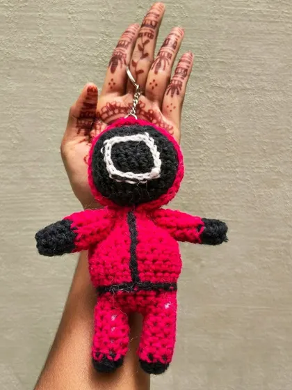 Holding the Squid Game guard keychain to show its size. It's a substantial, high-quality amigurumi piece.