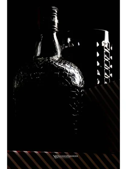 A fine art approach to liquor photography, using shadows and rim lighting to outline the distinct shape of a whiskey bottle and shaker. This style creates a sophisticated and mysterious feel.