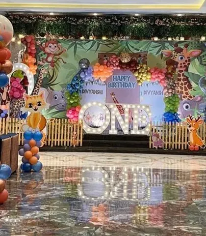 A wide shot of the premium jungle-themed first birthday party. This view shows the full stage, balloon columns, and the spacious banquet hall setting.