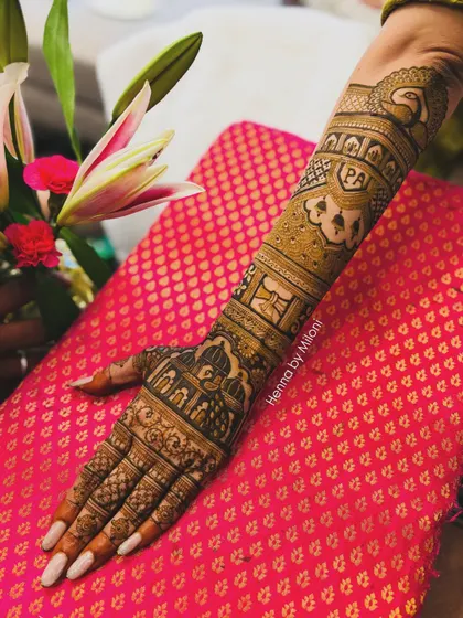 A personalized bridal arm design with the couple's initials "PA" inside a heart. The rest of the arm features traditional motifs like elephants and architectural domes.