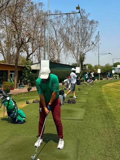 A golfer in a green shirt takes a practice swing, fully focused on his next shot.