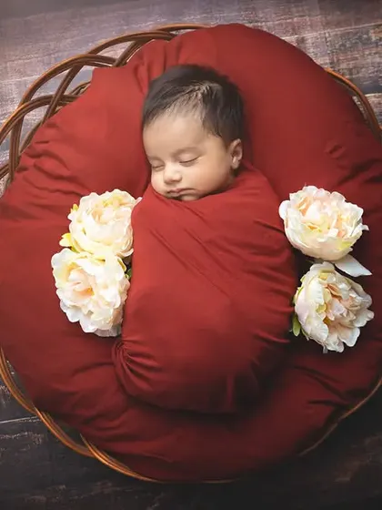 A newborn wrapped in deep red fabric sleeps on a matching cushion inside a rustic basket, creating a warm and cozy portrait.