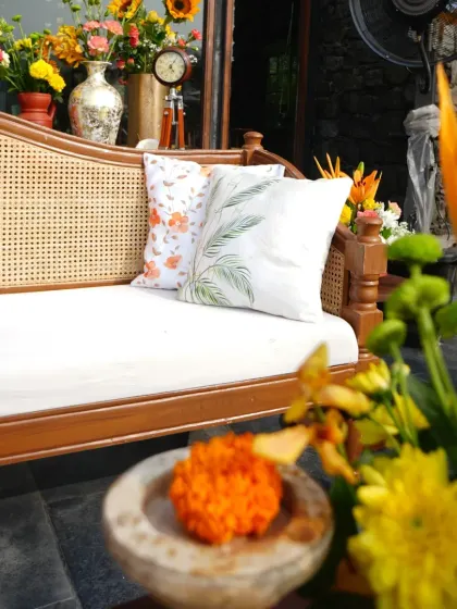 A cozy seating area at a Haldi, with a traditional wooden cane sofa, printed cushions, and surrounded by bright yellow and orange flowers.