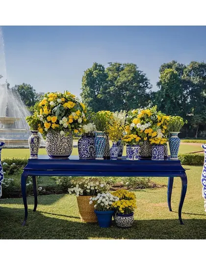 A beautiful console table decorated with blue pottery vases and bright yellow flowers, set against a garden backdrop. A perfect fusion of elegance and nature.