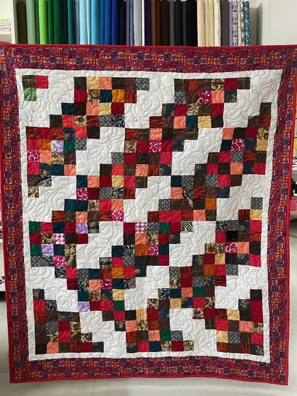 A scrappy quilt in a "trip around the world" pattern, using a warm palette of reds, oranges, and browns.