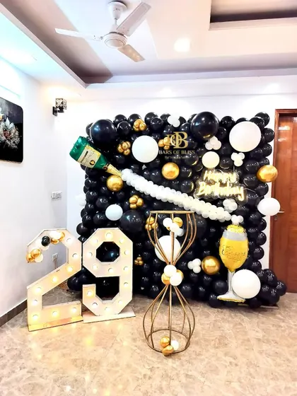 A sophisticated champagne-themed birthday party. This unique setup includes a wall of black, white, and gold balloons with a champagne bottle balloon pouring out "bubbly" white balloons, complemented by '29' marquee numbers.