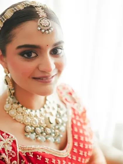 A classic, elegant bridal portrait. The bride looks directly at the camera with a soft smile, her beauty illuminated by the natural light from the window.
