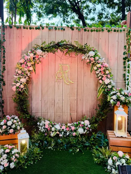 A rustic-chic photo booth with a large wreath of greenery and pastel flowers. The couple's initials monogram in the center adds a personalized touch to the wooden backdrop.