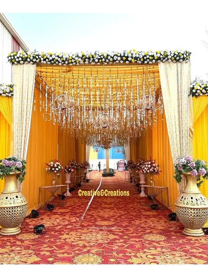 A beautiful yellow-themed entrance with hanging crystals and chandeliers. The large brass vases add a touch of traditional elegance to the modern setup.