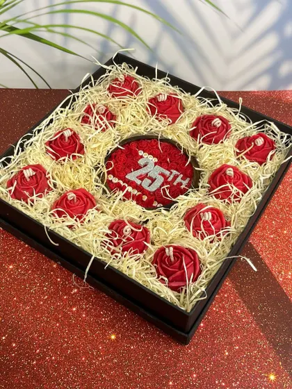 This is a custom anniversary gift box I created, featuring a central candle personalized with '25th' and surrounded by smaller rose candles. It showcases my ability to create bespoke gifts for milestone celebrations.