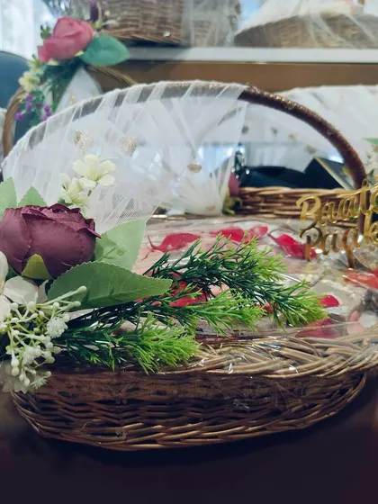 A classic wicker basket filled with gifts, wrapped in delicate white tulle and adorned with flowers. This style of trousseau packaging is timeless and can be customized with different floral arrangements to match your theme.